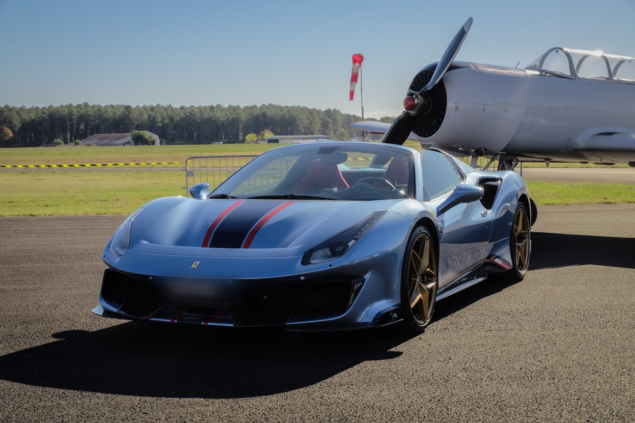 Ferrari 488 Pista Spider bleue sur tarmac d'aérodrome, avion d'entraînement à hélice en arrière-plan
