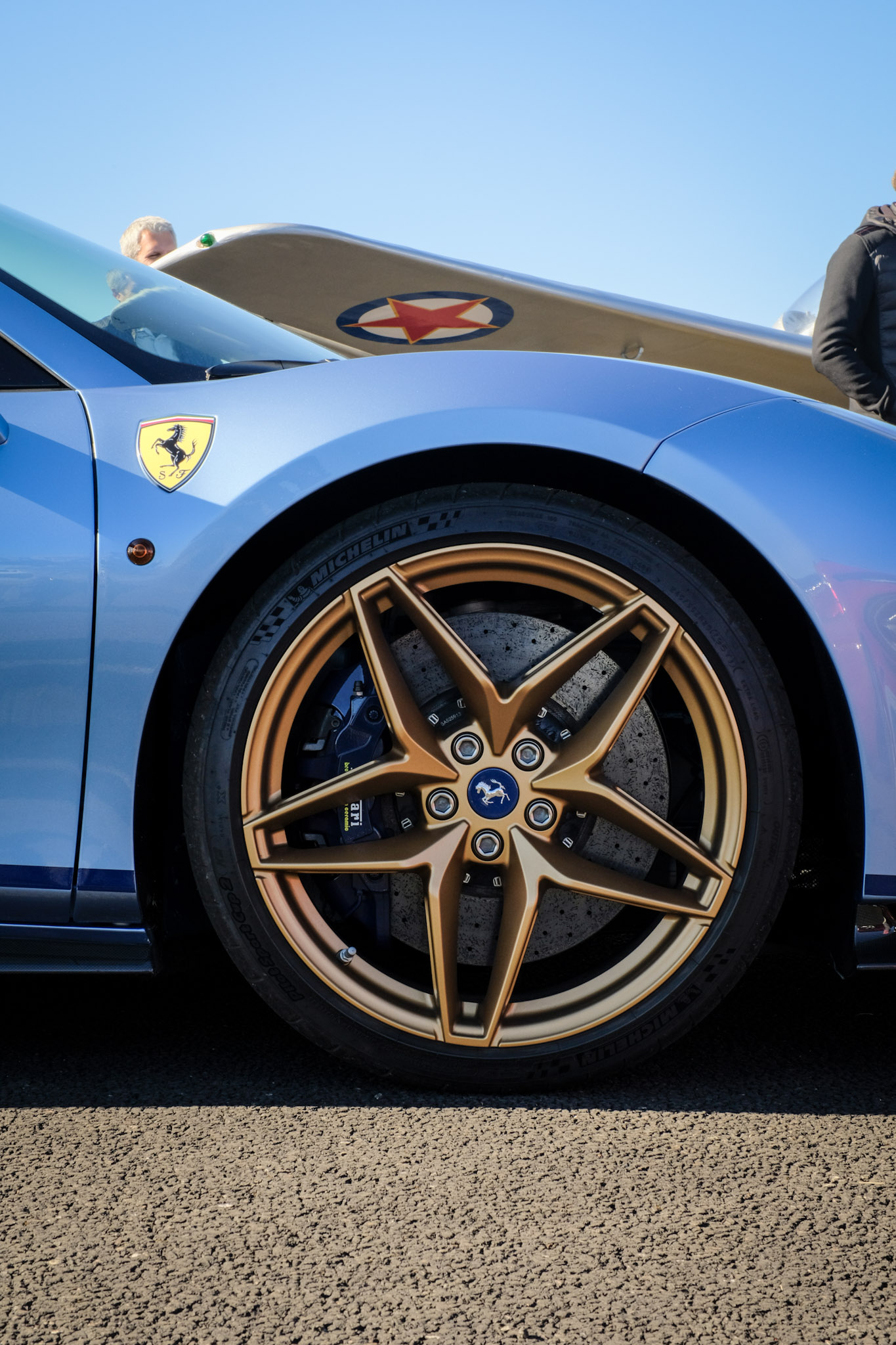Jante 5 branches bronze Ferrari 488 Pista Spider — étrier bleu, bouclier Scuderia Ferrari jaune sur l'aile, avion en fond