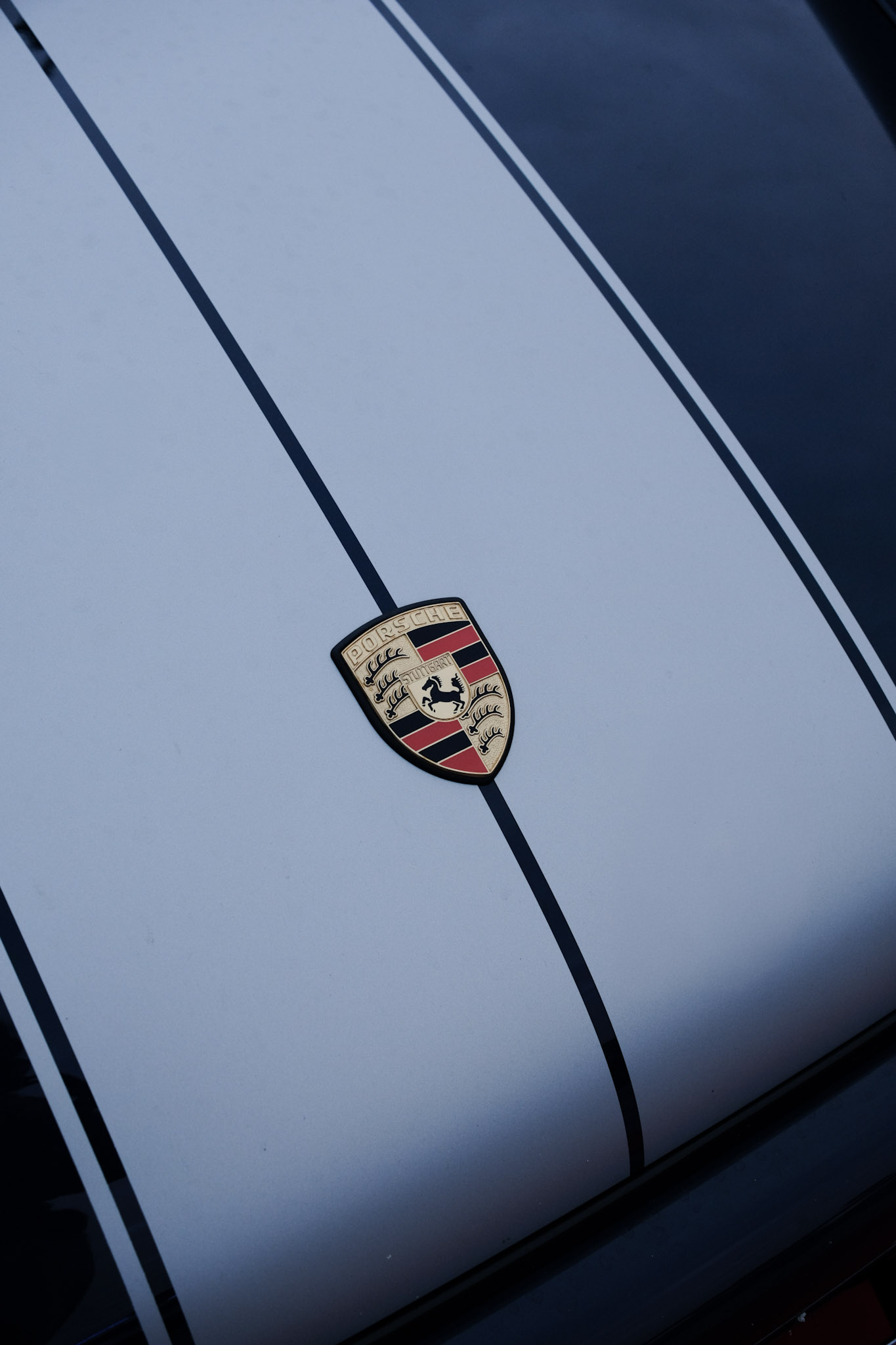 Capot avant Singer — écusson Porsche centré sur la bande grise entre deux filets sombres